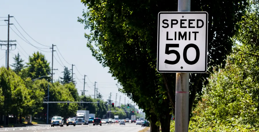 50 mph speed limit sign on post with a road and tree